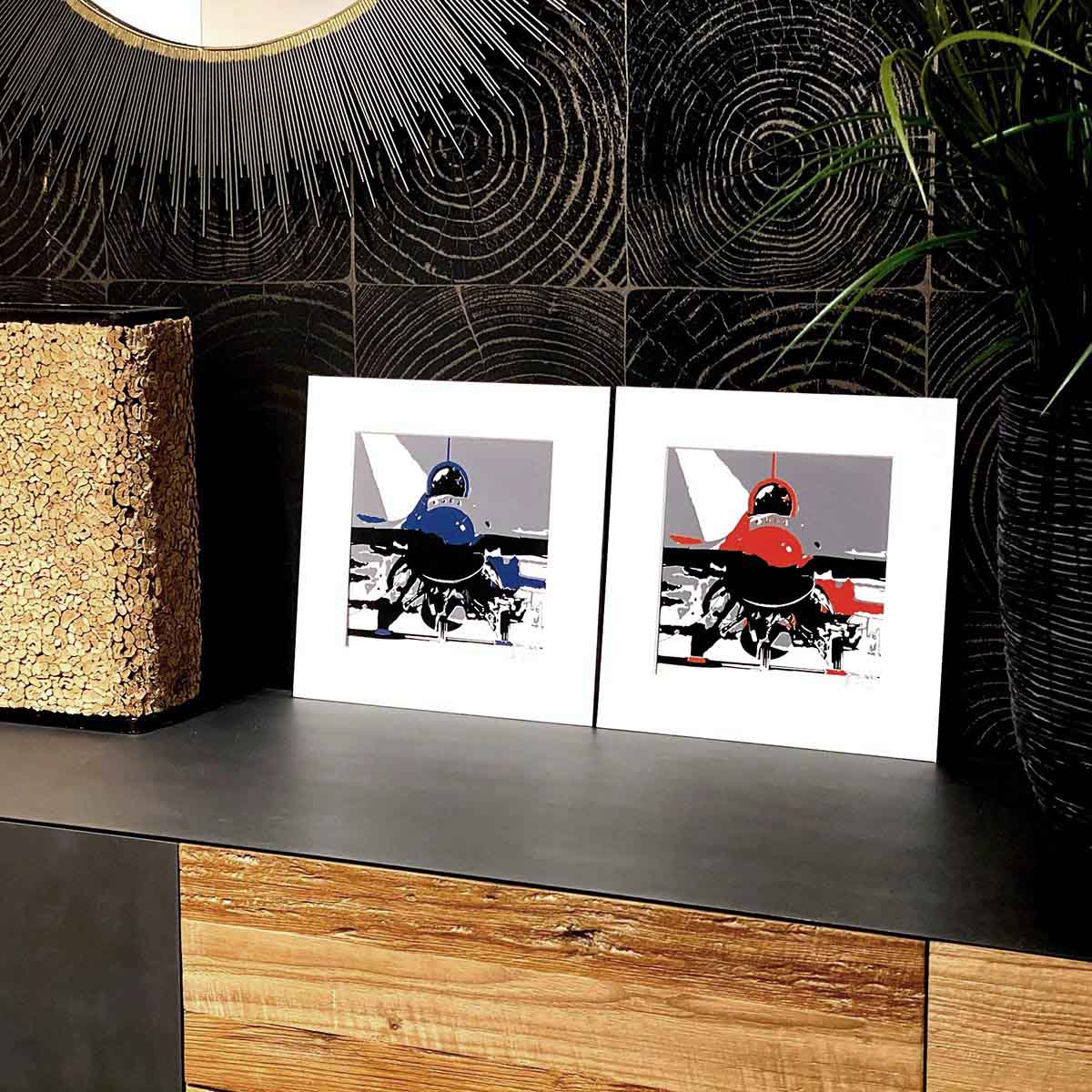 Three colour screen prints, red or blue, black and grey, of a Lockheed Martin F-16 on a brown desk.