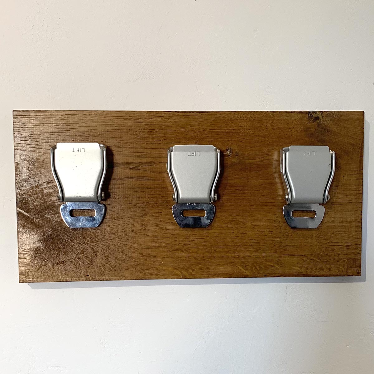 Three buckles of an airline seatbelt on an oak board.