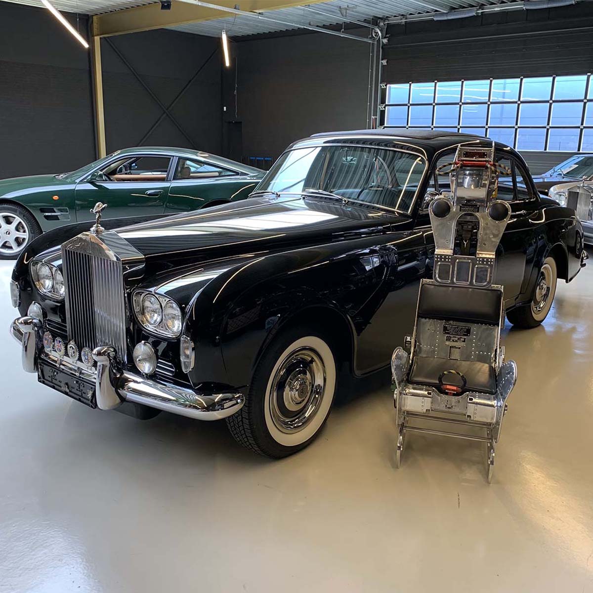 Polished Martin-Baker ejection seat next to a Rolls-Royce and an Aston Martin.