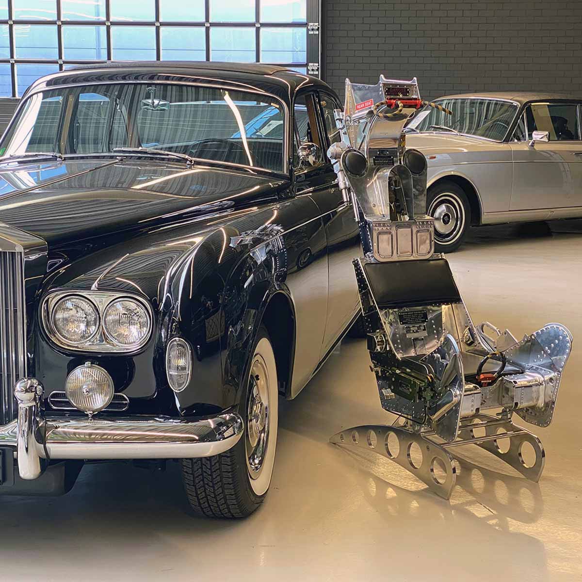 Polished Martin-Baker ejection seat next to two Rolls-Royce cars.