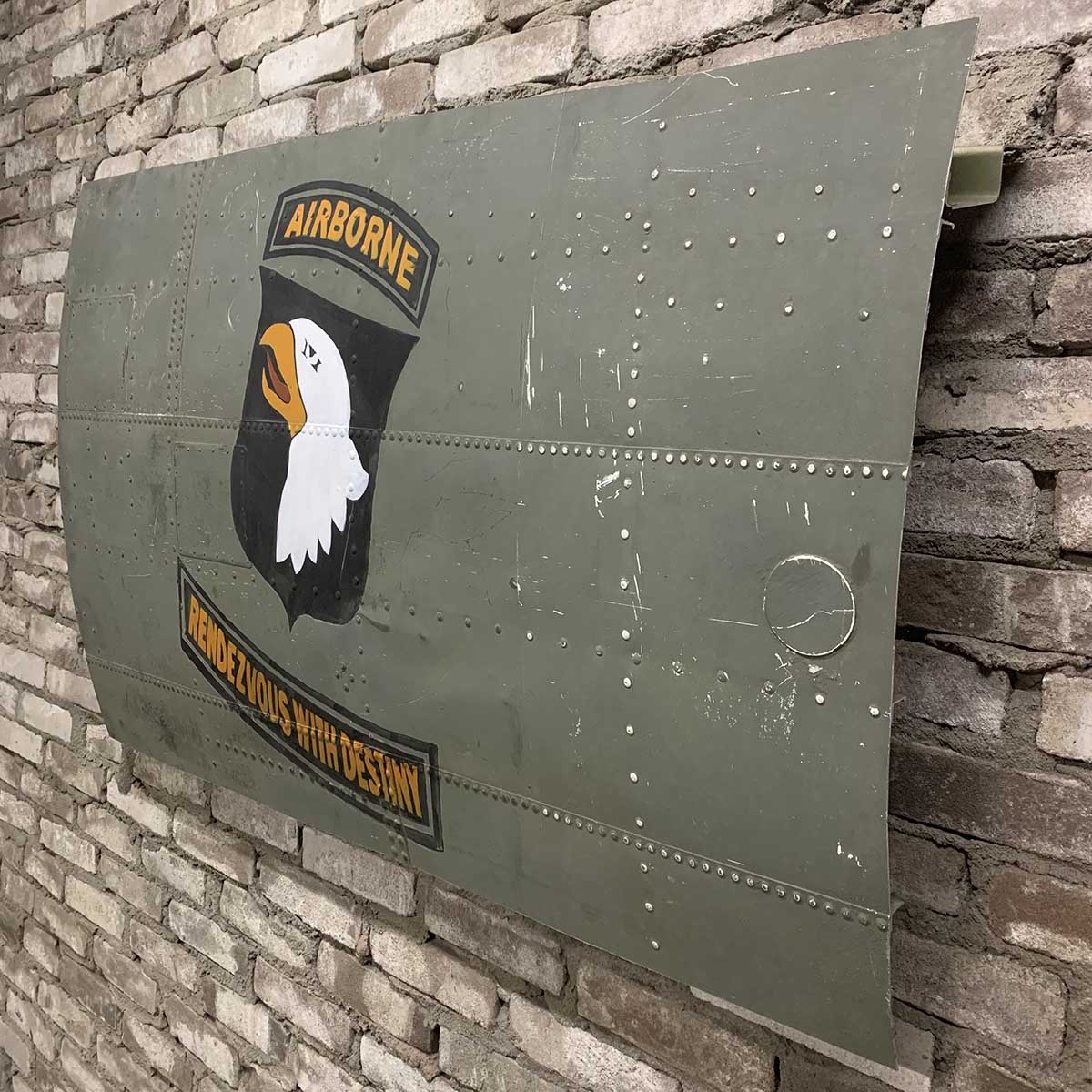 Original C-47 Dakota skin panel painted with Rendezvous with Destiny nose art hanging on a brick wall.