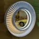 Mirror made from a Pratt & Whitney jet engine stator hanging on a brick wall in Kaeve, reflecting a Porsche car.