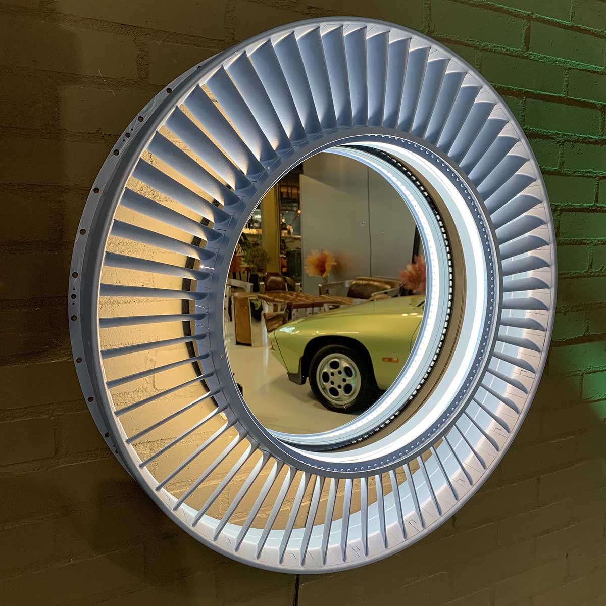Mirror made from a Pratt & Whitney jet engine stator hanging on a brick wall in Kaeve, reflecting a Porsche car.